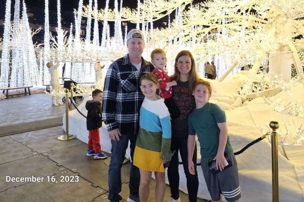family standing in front of light up christmas trees outside