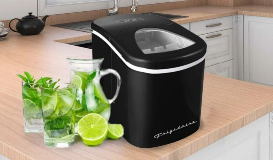a blakc counter top icemaker sitting next to a pitcher of limade