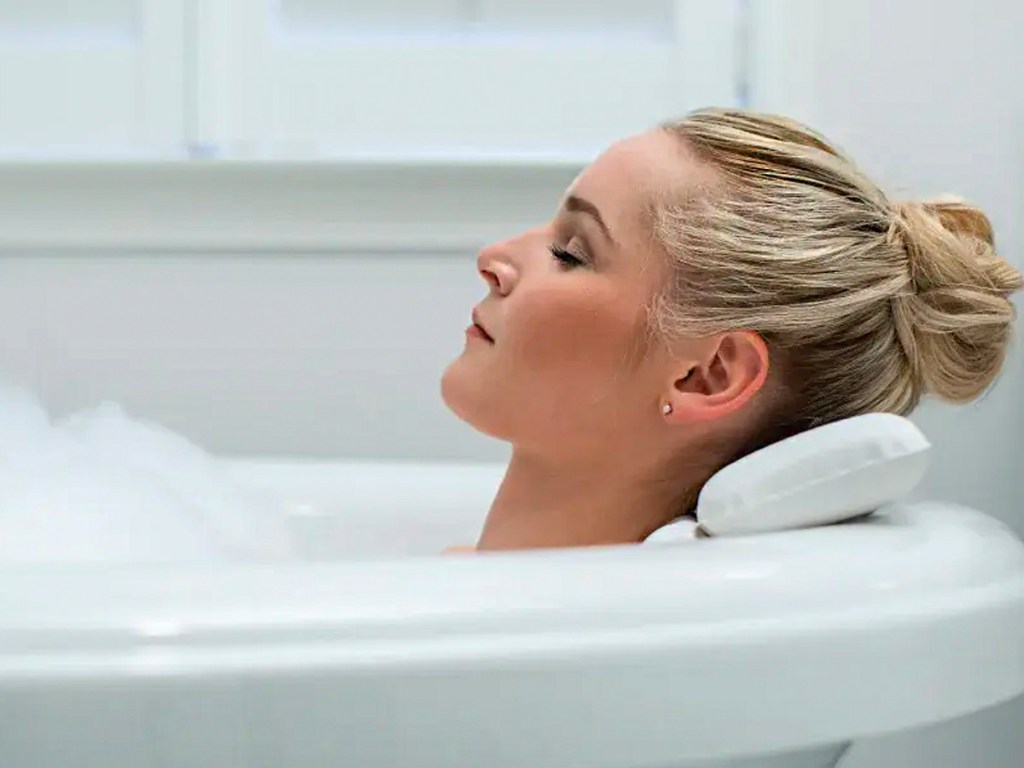 blonde woman laying head on white bath pillow