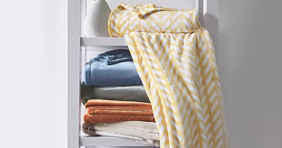 throw blankets stacked on shelf with yellow and white chevron blanket laying on top 