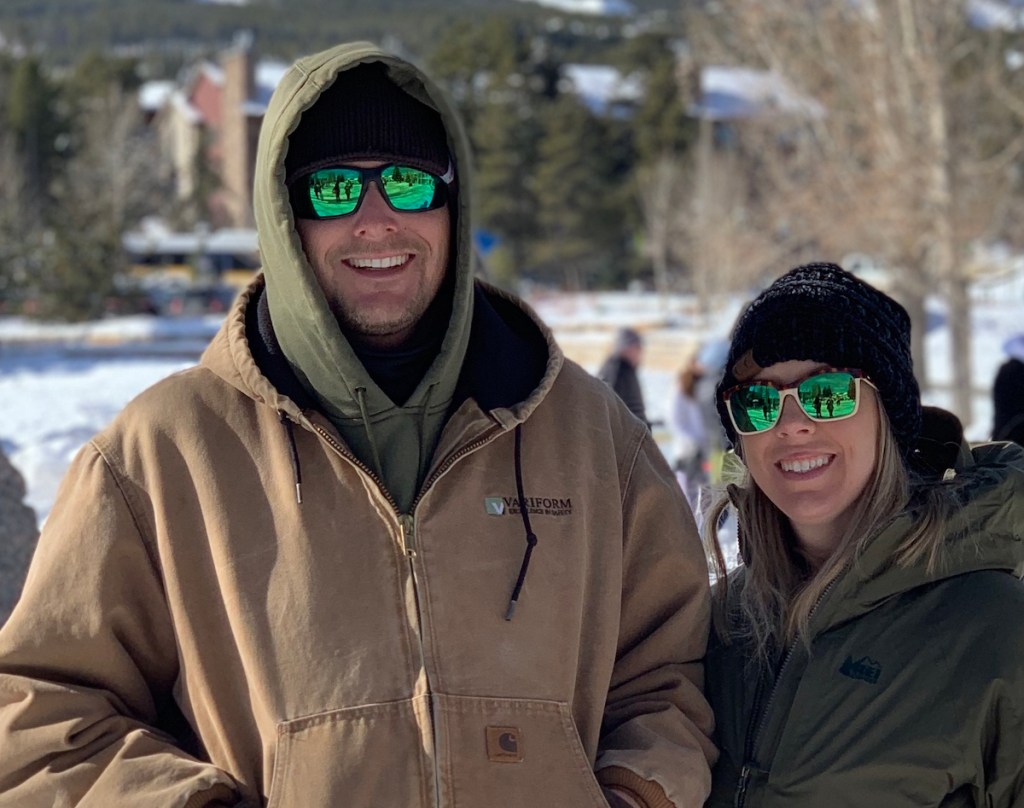 man and woman standing outside in snow wearing green sunglasses