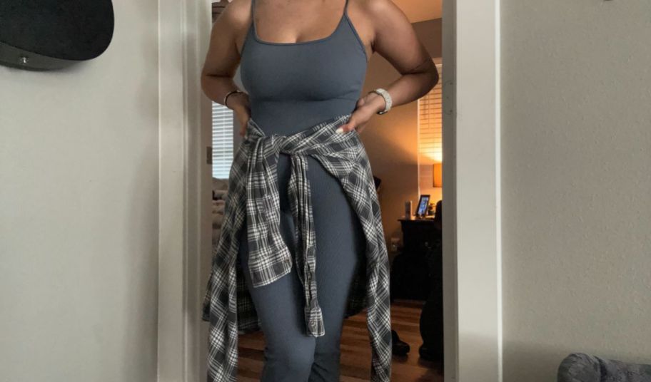 a woman wearing a dark gray tanktop jumpsuit with a plaid shacket tied around the waist