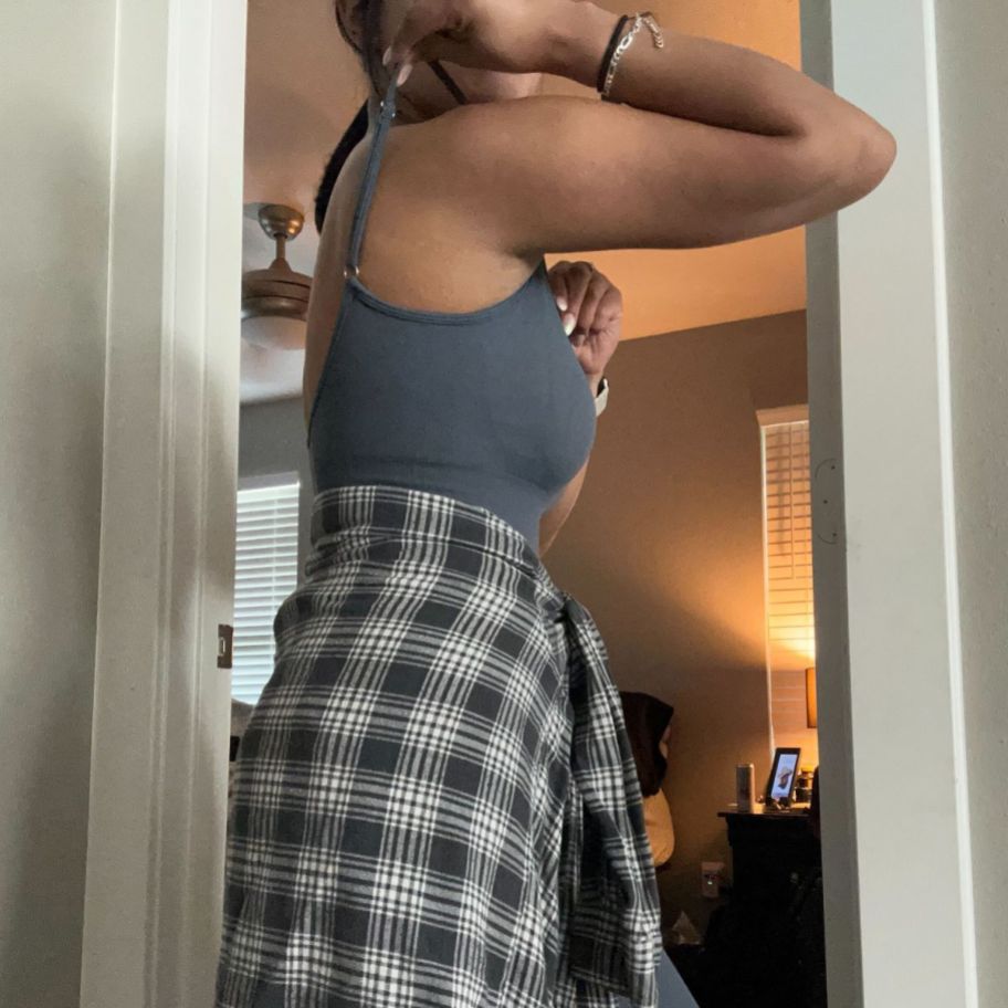 side view of a woman wearing a dark gray tanktop jumpsuit with a plaid shacket tied around the waist