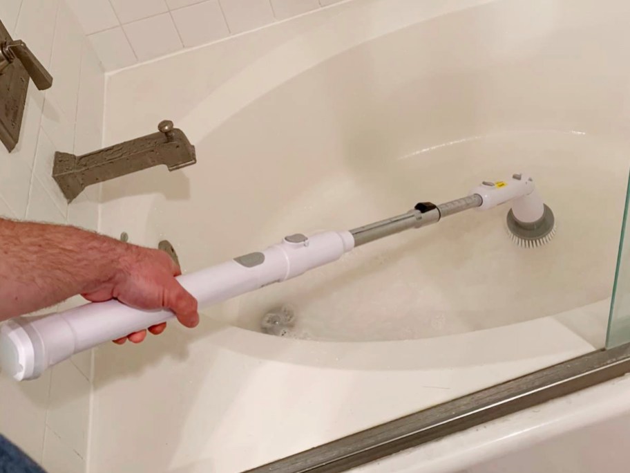 person using white and gray electric spin brush cleaning bathtub
