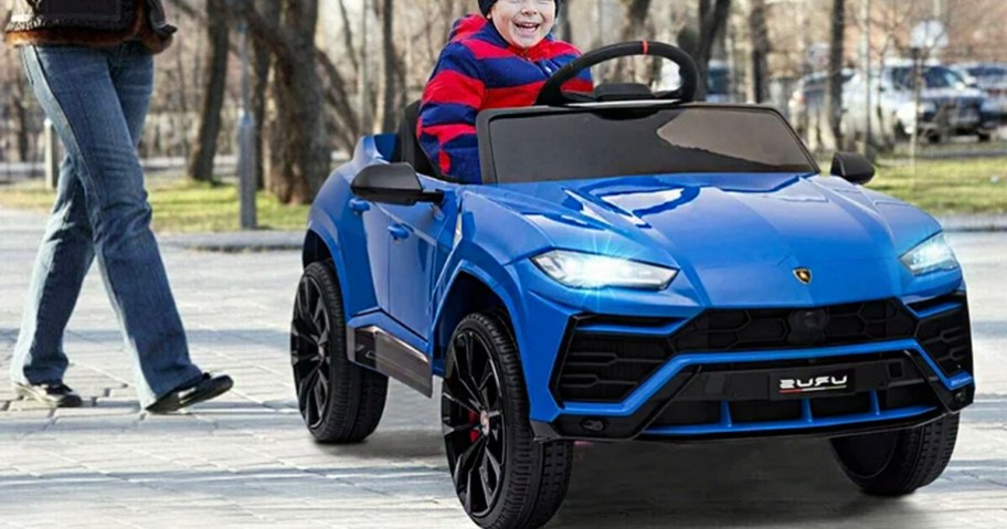 boy riding in blue lamborghini rideon car on sidewalk with parent walking behind it