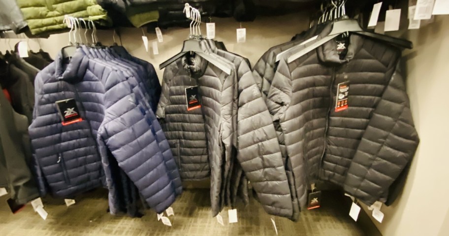 men's navy, grey, and black mid-weight puffer jackets hanging on a wall display at Kohl's