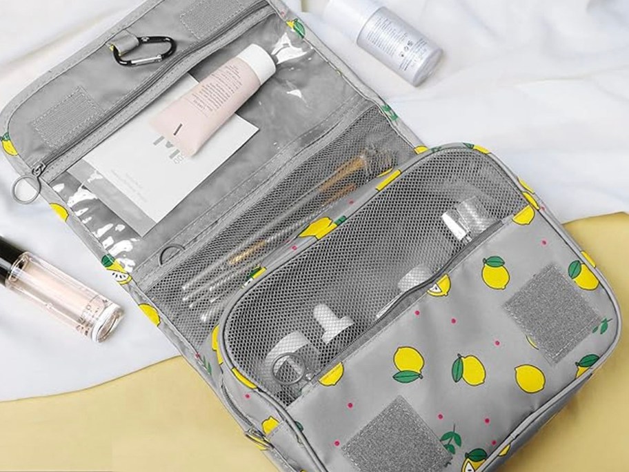 gray toiletry bag with lemon print and makeup/brushes inside on it laying on table 