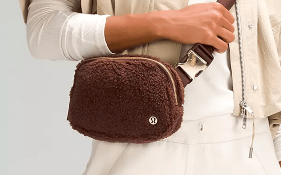 person wearing brown fleece belt bag with hand grabbing strap