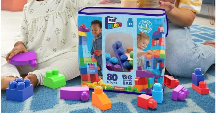 little girl playing with MEGA BLOKS with mom next to her, large bag of MEGA BLOKS between them