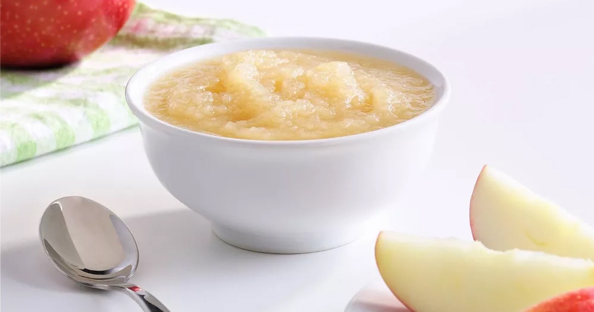 mott's applesauce in white bowl on table next to spoon and apple slice