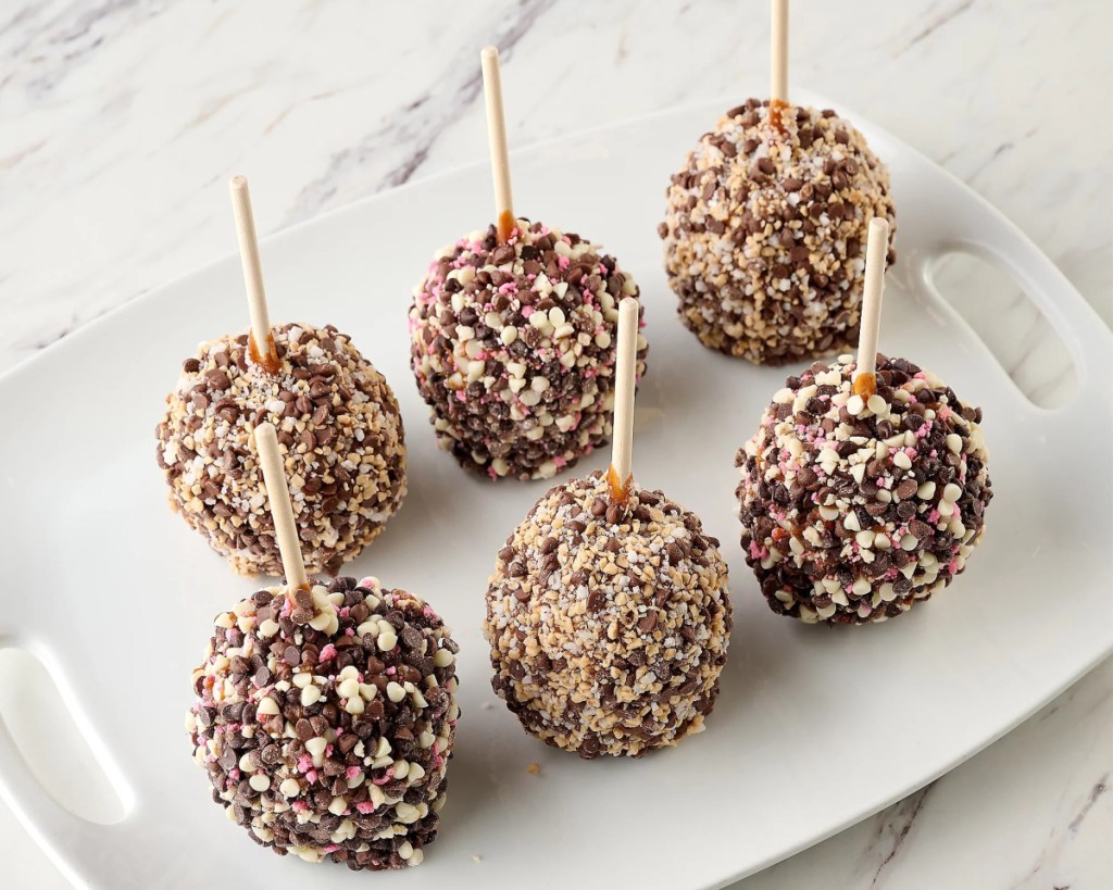 six candy coated caramel apples on a tray