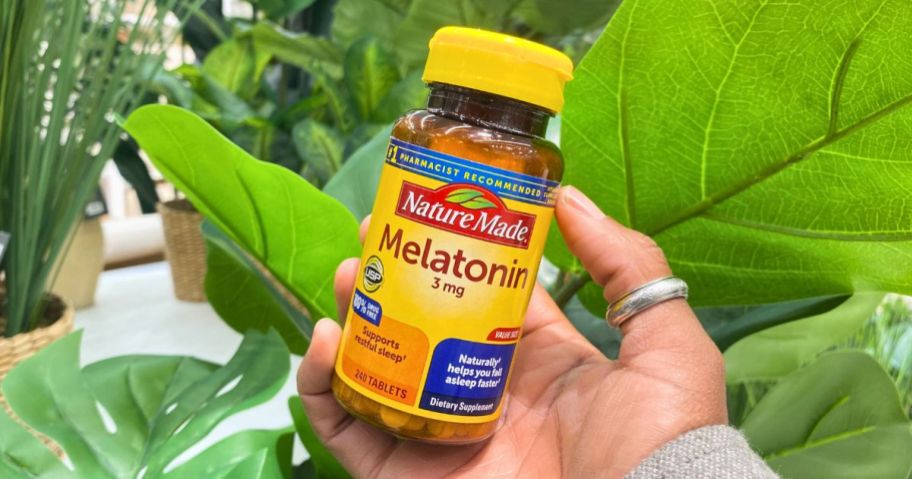 a womans hand holding a bottle of nature made melatonin