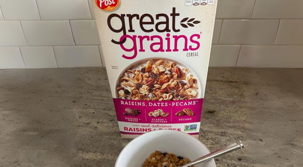 a box of post great grains cranberry almond crunch cereal, on a counter with a bowl of cereal in front of it