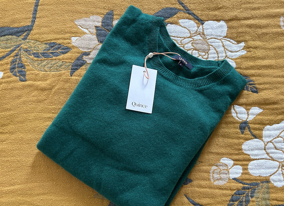 hunter green sweater folded on yellow floral blanket with quince tag