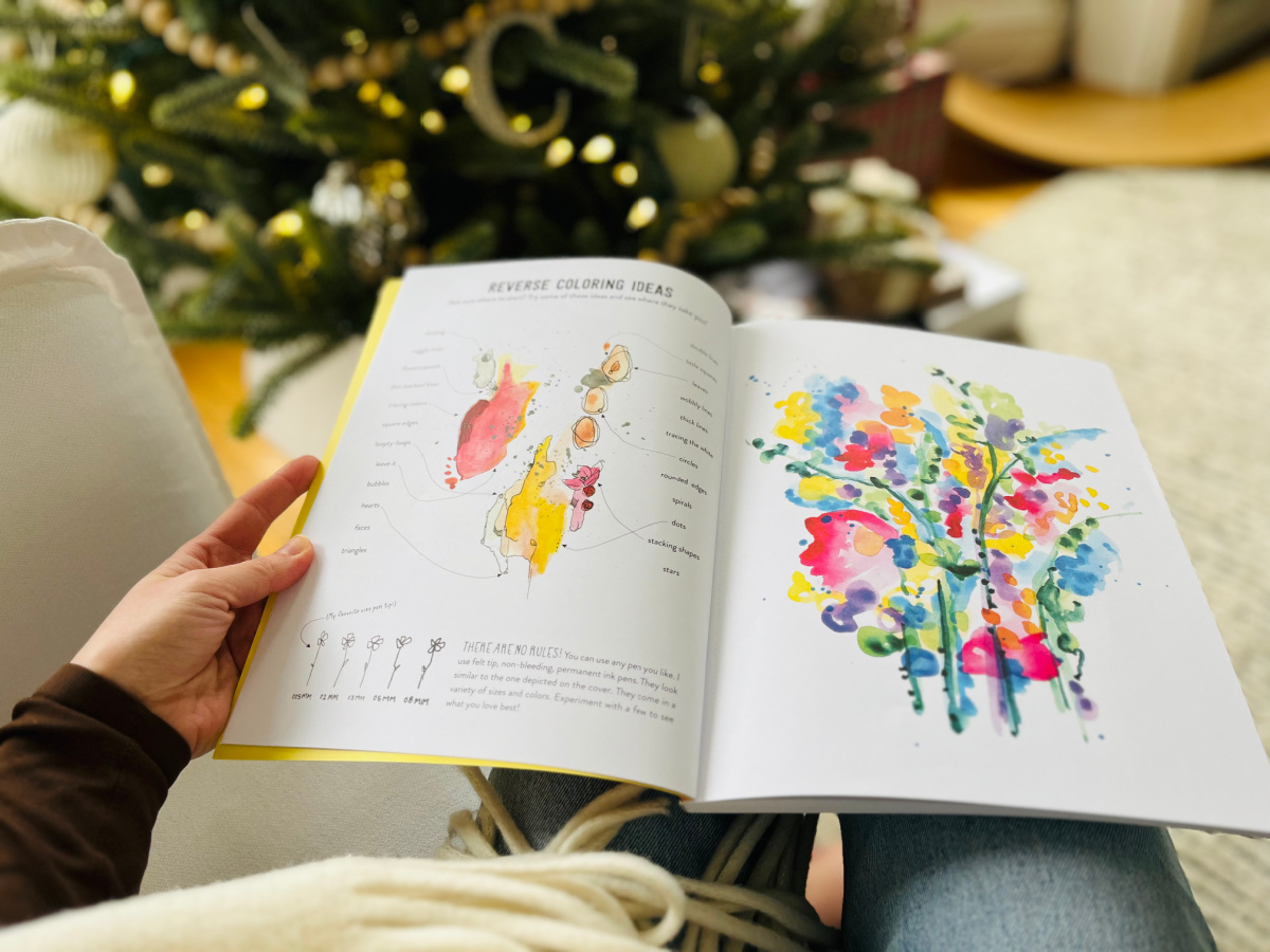 person sitting in a chair with an open coloring book on their lap and a christmas tree in the background