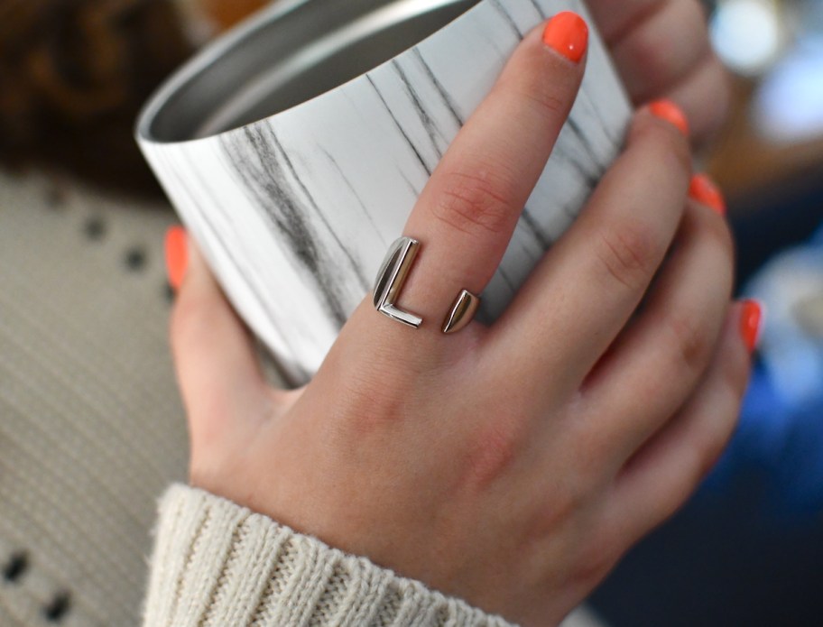 close up of hand with silver l initial ring holding marble mug