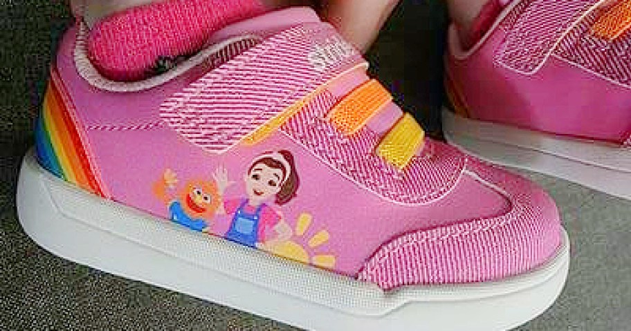 Pink children's sneakers with rainbow stripes feature animated characters from Ms. Rachel and a sun design.