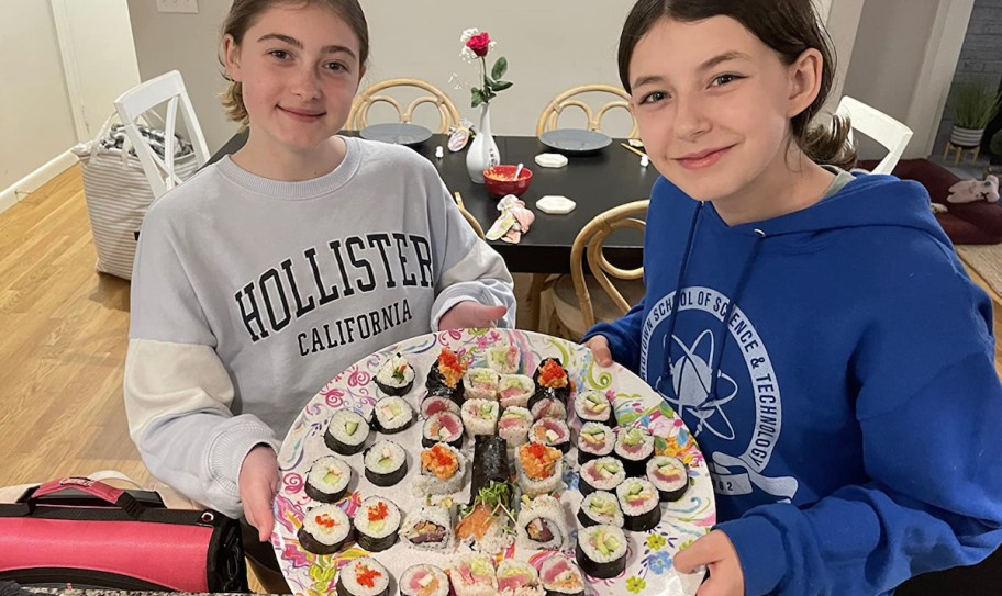 two teen girls holding a plate of sushi