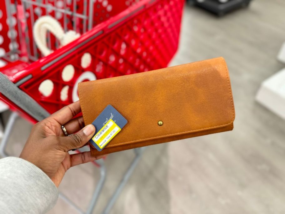 hand holding a tan leather looking fold over women's wallet, Target cart in the background