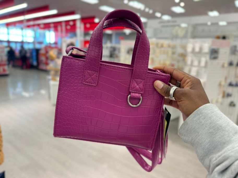 hand holding a small purple handbag with straps
