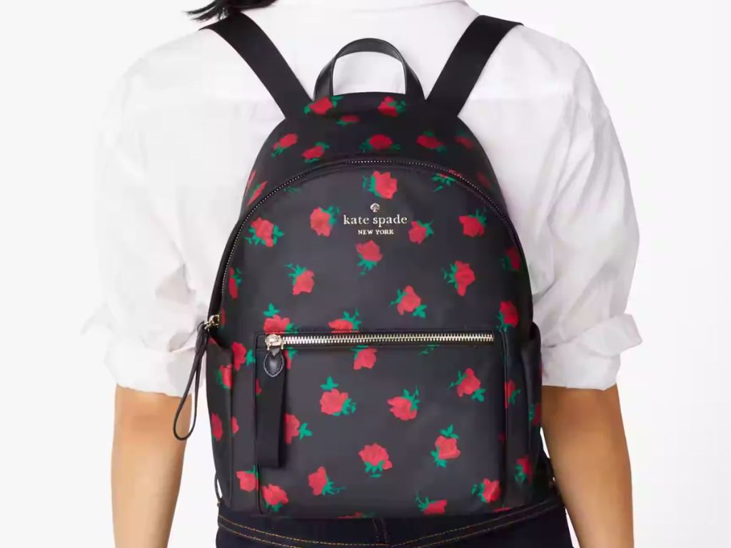 back of a woman shown wearing a Kate Spade backpack bag in black with red roses