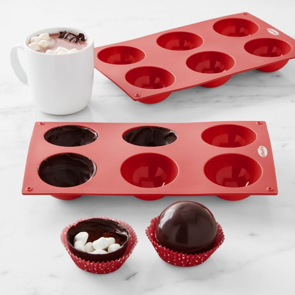 two red Hot Chocolate Bomb Molds with some filled and some made and cup of coffee