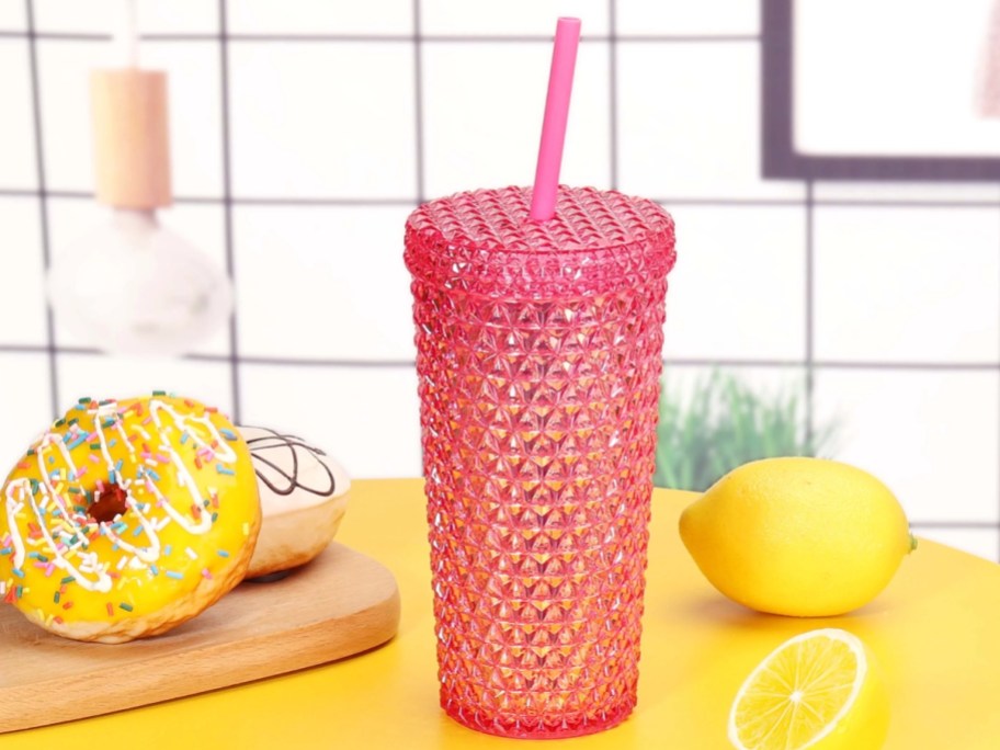 small pink studded tumbler with straw beside of lemons and donuts