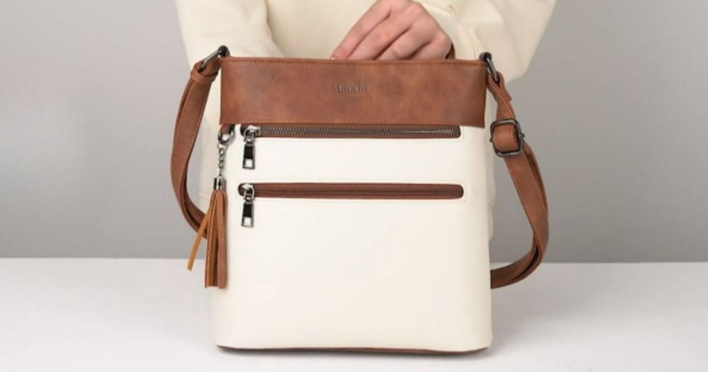 woman's hand on a cream and brown faux leather crossbody bag that's on a table