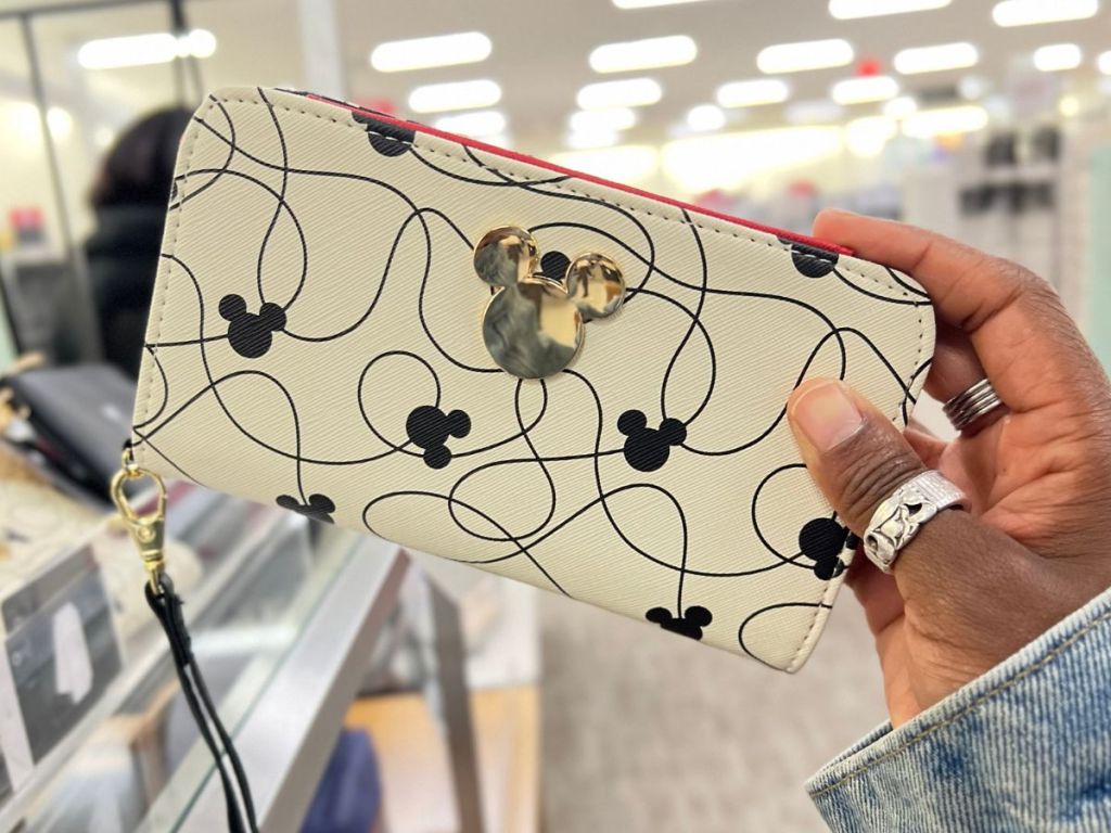 hand holding a cream, black and gold Mickey Mouse Wallet in store
