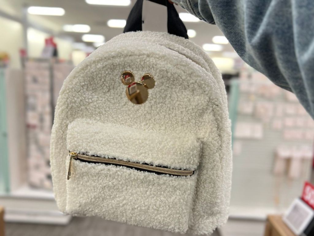 hand holding a white fuzzy fleece look Disney Mickey Mouse mini backpack in store