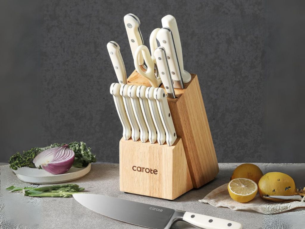Carote stainless steel knife set with white handles shown in wood block with chef's knife and food laying around it