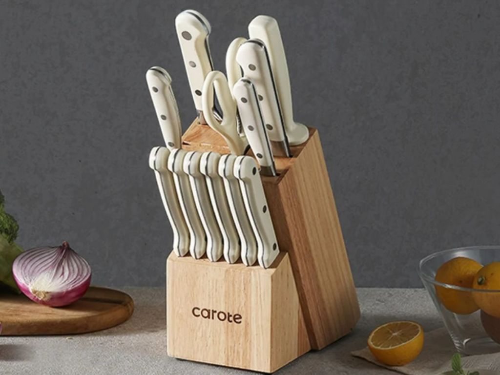 Carote stainless steel knife set with white handles shown in wood block with food laying around it