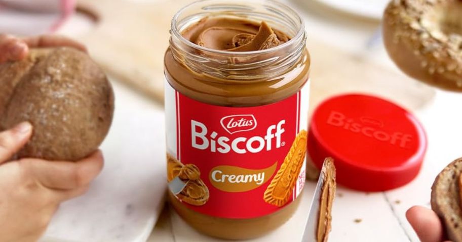 open jar of Lotus Biscoff Cookie Butter Spread on table with people and food around it