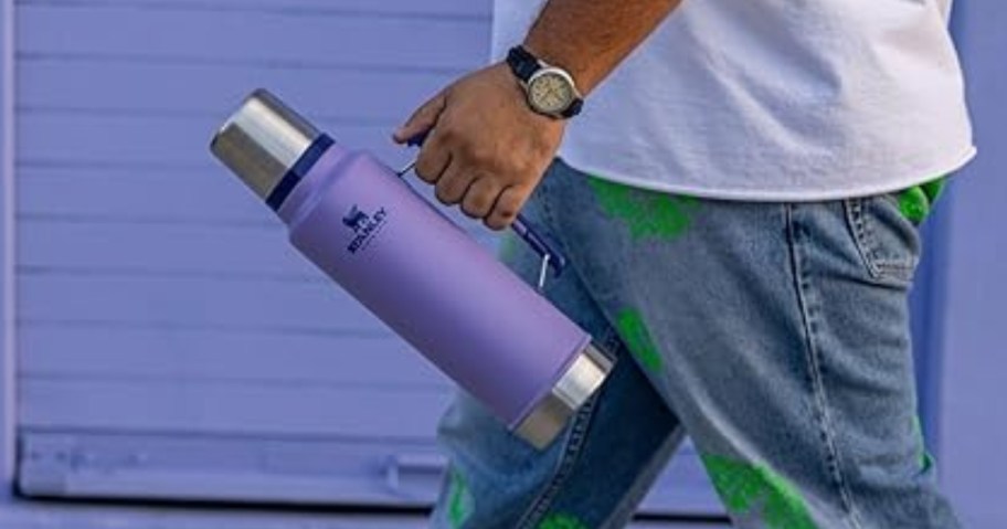 man walking down the street carrying a Lavender Stanley bottle / thermos