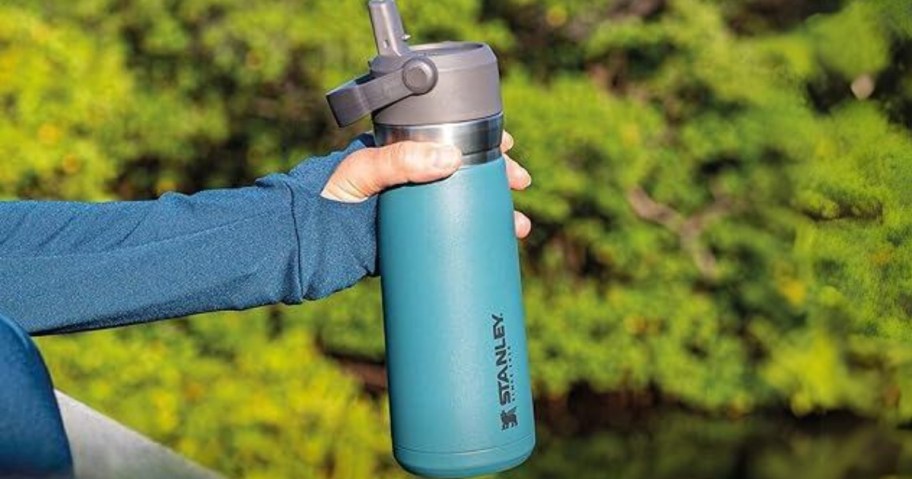 hand holding a teal blue Stanley flip top water bottle with handle