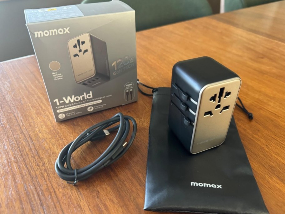 MOMAX 120W GaN Universal Travel Adapter in silver and black shown with the box, usb cable and carry bag sitting on a table