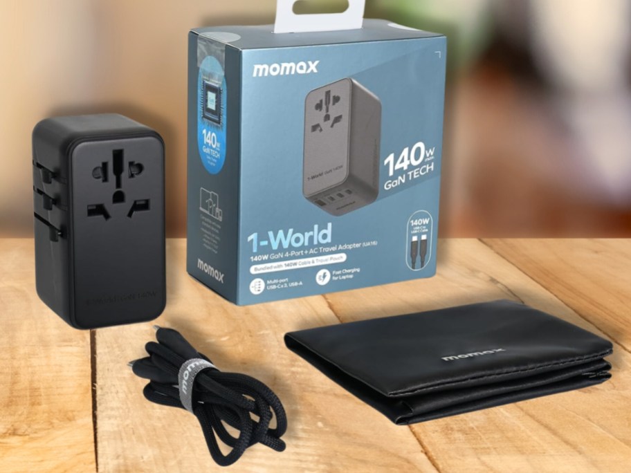 MOMAX 140W GaN Universal Travel Adapter in black shown with box, usb cord and travel bag on a table