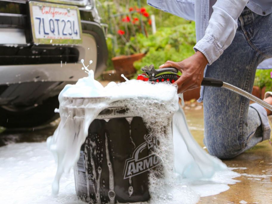 woman filling an Armorall bucket with soapy water next to a car