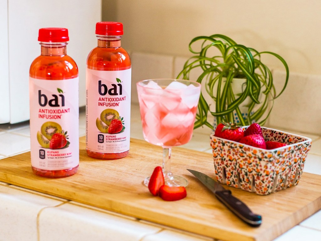 two Bai Kupang Strawberry Kiwi drinks on cutting board with sliced strawberries