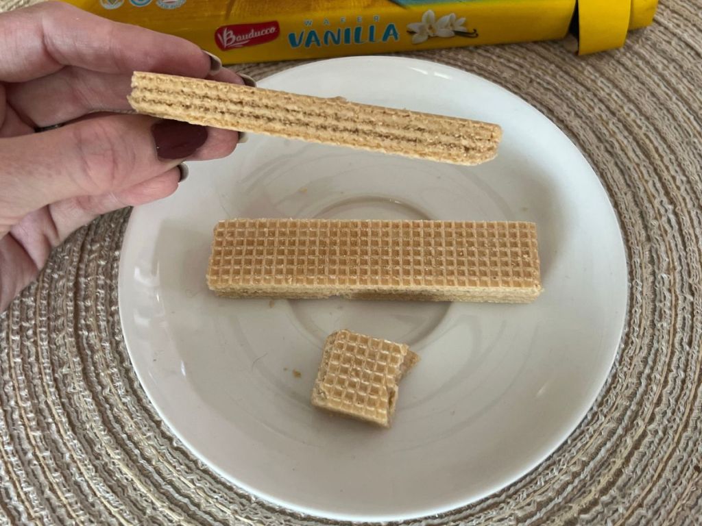 Bauducco Vanilla Wafers on a late with a hand holding one up up to show the view from the side