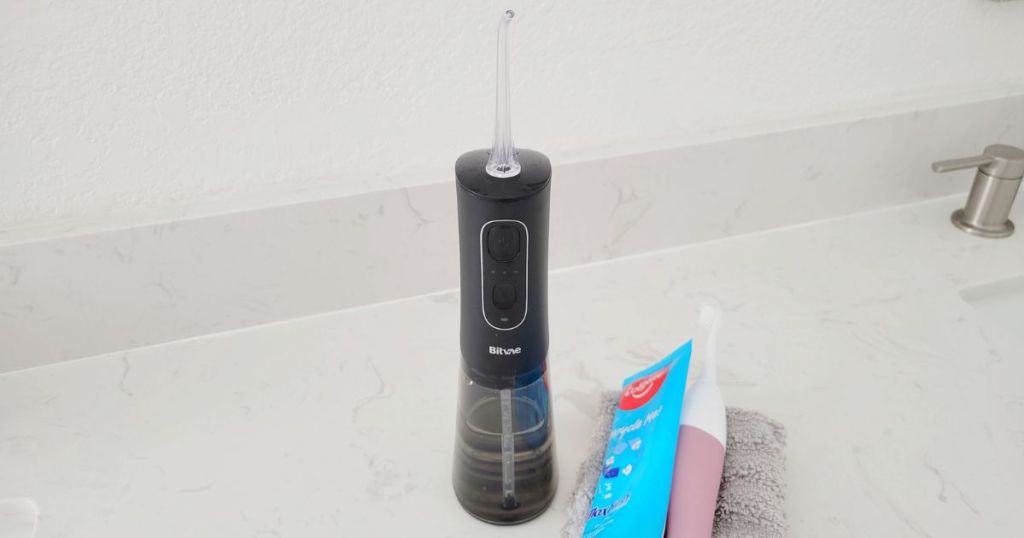 black water flosser on white marble counter next to toothpaste and pink electric toothbrush