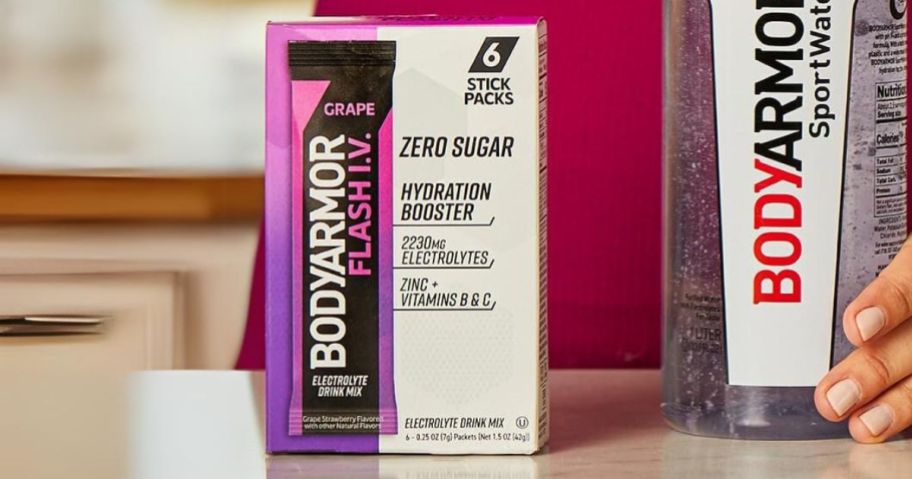 a box of grape flavored bodyarmor electrolyte drink mix on a counter next to a bottle of bodyarmor water
