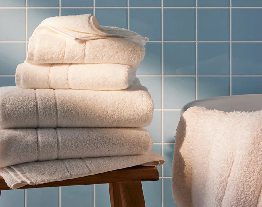 stack of cream colored bath towels on wood bench in bathroom with blue towels