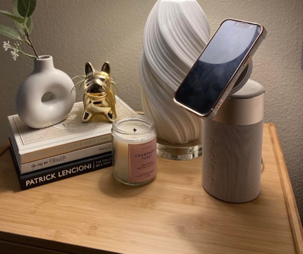 Speaker and MagSafe phone charger sitting on nightstand with books, candle, and lamp 