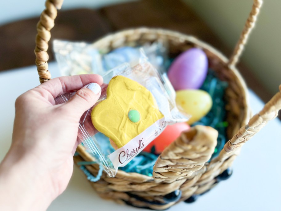 hand placing a yellow flower cookie into easter basket