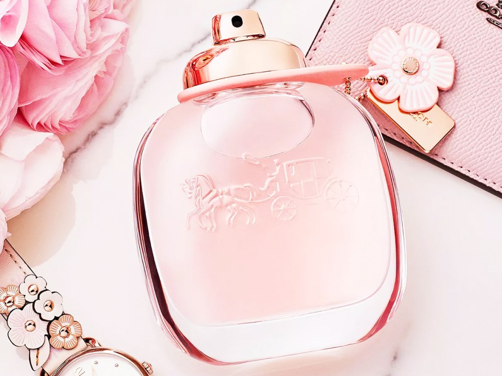 pink bottle of coach perfume on its side near pink cardholder and floral watch