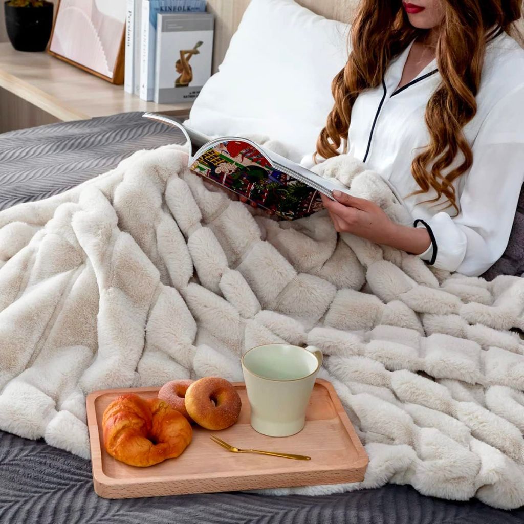a woman reading a book while covered up with a beige Faux Fur Blanket with breakfast tray in bed.