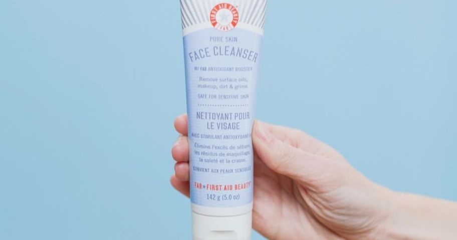 Hand holding a tube of First Aid beauty Cleanser