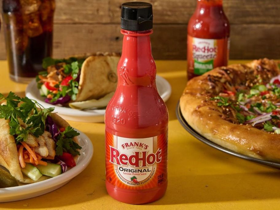 A bottle of Frank's RedHot on a table surrounded by food 