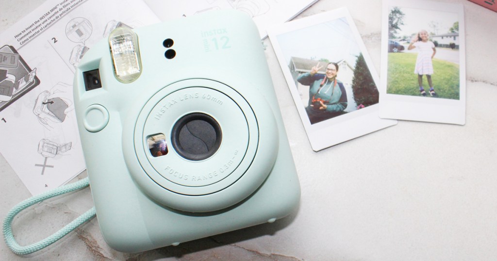 light blue Fujifilm Instax Mini 12 camera next to Polaroids